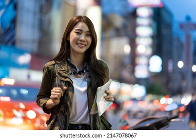 Portrait Of Asian Attractive Woman Backpacker Travel In City At Night. Young Woman Tourist Traveler Stand In Beautiful Street Enjoy Spend Time On Holiday Vacation Trip In Thailand And Look At Camera.