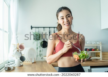 Portrait of Asian attractive woman hold salad bowl and look at camera. Beautiful sport girl in sportswear enjoy eat clean vegetables after exercise for health in house. Diet and Healthy food concept. Сток-фото © 