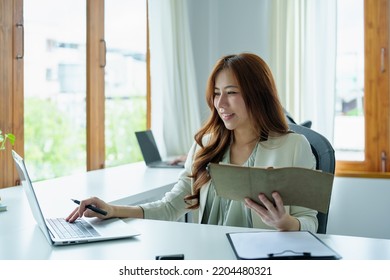 Portrait Of An Asian Bank Employee Using Notebooks To Take Notes, Budget Documents And Computers To Close Financial Statements.