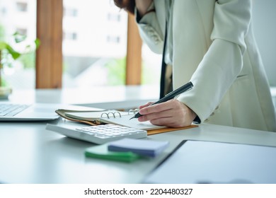 Portrait Of An Asian Bank Employee Using Pen Tonotepad , Calculator  And Computer To Working