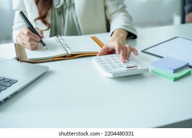 Portrait Of An Asian Bank Employee Using A Financial Budget Calculator, Notepad  And Computer To Working.