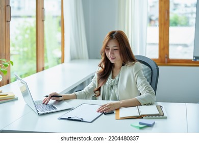 Portrait Of An Asian Bank Employee Using A Computer And Documents To Manage Financial Statements.