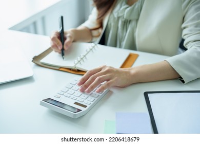 Portrait Of An Asian Bank Employee Using A Financial Budget Calculator, Notepad  And Computer To Working.