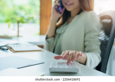 Portrait Of An Asian Bank Employee Using A Financial Budget Calculator, Notepad, Telephone And Computer To Working.