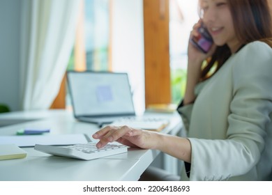 Portrait Of An Asian Bank Employee Using A Financial Budget Calculator, Notepad, Telephone And Computer To Working.