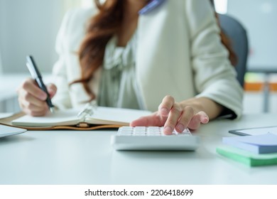 Portrait Of An Asian Bank Employee Using A Financial Budget Calculator, Notepad  And Computer To Working.