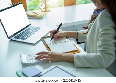 Portrait Of An Asian Bank Employee Using A Financial Budget Calculator, Notepad  And Computer To Working.