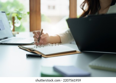 Portrait Of An Asian Bank Employee Using Notebooks To Take Notes, Budget Documents And Computers To Close Financial Statements.