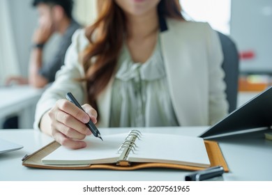 Portrait Of An Asian Bank Employee Using Notebooks To Take Notes, Budget Documents And Computers To Close Financial Statements.