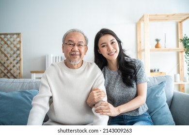 Portrait Of Asian Beautiful Daughter Hugging And Sit With Older Father. Attractive Woman Granddaughter Visit Senior Mature Man In House, Enjoy Spend Time Together In Living Room Then Looking At Camera