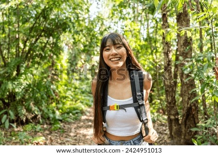 Portrait of Asian beautiful woman backpacker traveling alone in forest. Attractive girl traveler walk in nature wood with happiness and fun during holiday vacation trip then smiling, looking at camera