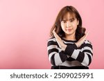 Portrait Asian beautiful young woman unhappy or confident standing wear holding two cross arms say no X sign, studio shot isolated pink background, Thai female pose reject gesture with copy space