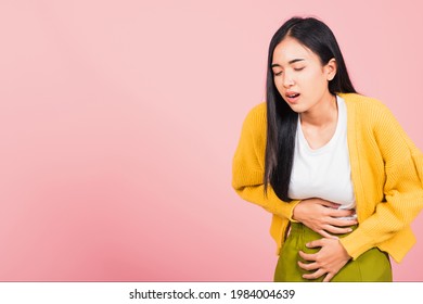 Portrait of Asian beautiful young woman has stomachache, female abdominal pain suffering from stomach ache, studio shot isolated on pink background, Health and medical gastritis concept