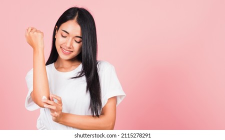 Portrait of Asian beautiful young woman applying lotion cosmetic moisturizer cream on her elbow skin, studio shot isolated on pink background, Healthcare medical and hygiene skin body care concept