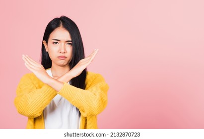 Portrait Asian beautiful young woman unhappy or confident standing wear holding two cross arms say no X sign, studio shot isolated pink background, Thai female pose reject gesture with copy space