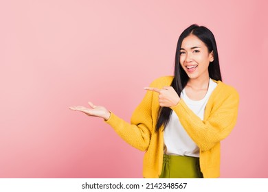 Portrait Asian beautiful young woman smiling standing pointing finger out on pink background, Thai happy face excited female point into empty looking to side away with copy space for text - Shutterstock ID 2142348567