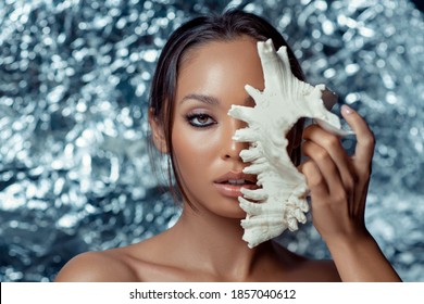 A Portrait Of An Asian Beauty Covering Half Of Her Face With A Large White Shell. Blurred Silver Background.