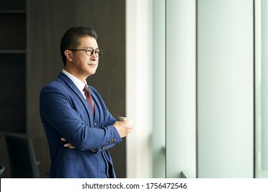 Portrait Of A Asian Business Leader Senior Manager Standing By Window Thinking