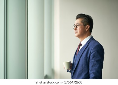 Portrait Of A Asian Business Leader Senior Manager Standing By Window Thinking