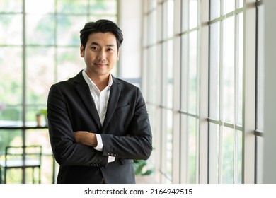 Portrait of Asian business man wear suit at the workspace office. Smiling Asian business man standing with arms crossed in background modern office - Powered by Shutterstock