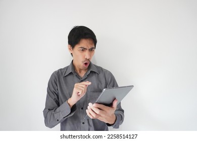 Portrait of Asian business person looking on tablet screen with a wow, crazy, shocked facial expression, isolated on grey background. Concept of male model posing amazement reaction in surprised face. - Shutterstock ID 2258514127