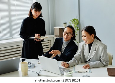 Portrait Of Asian Business Team Of Three People Looking At Computer Screen And Smiling While Enjoying Work In Office