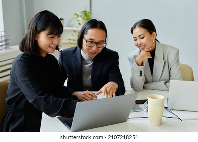 Portrait Of Asian Business Team Of Three People Looking At Laptop Screen And Smiling While Meeting In Office