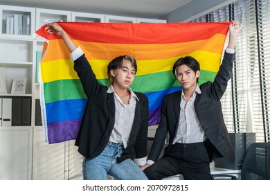 Portrait Of Asian Businessman Gay Hold LGBTQ Flag In Office Workplace. Attractive Man Colleagues In Formal Suit Have Fun Enjoy Work In Corporate With Gay Pride And Confidence. Homosexual-LGBTQ Concept