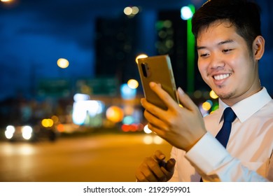 Portrait Asian Businessman Typing An Sms Message Via Smartphone After Work Near Office At Night City Street, Bokeh Lights, Young Man Walking And Chatting With Friends At Social Networks Outdoor