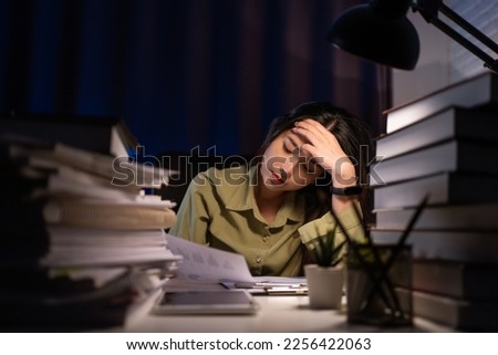 Portrait of Asian Businesswoman sitting and working hard at with front of computer and lots of documents on the table in workplace at late with serious action, Work hard and too late concept