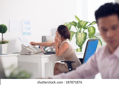 Portrait of Asian businesswoman speaking on the phone and receiving fax