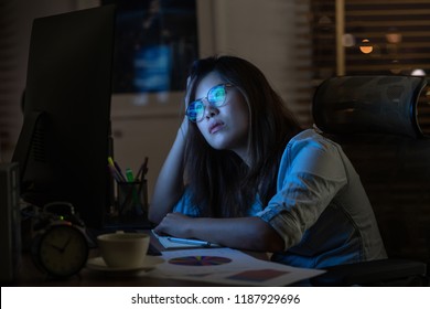 Portrait of Asian Businesswoman working hard and looking the digital graphic on the table with front of computer desktop in workplace at late with serious action, Work hard and too late concept