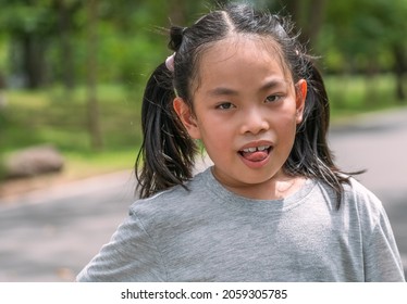 Portrait Asian child girl in the park, many sweats on the face,  tongue out to show tired, gray color t-shirt, blurred background of trees in the park, sunlight image.