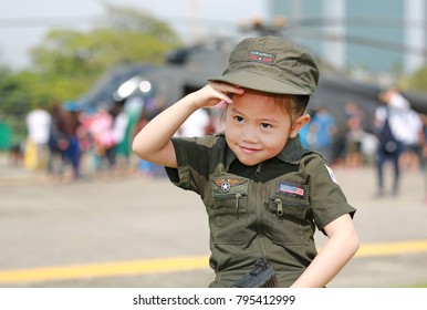 Portrait Of Asian Child Girl Wearing Airforce Pilot Suit Against Blur Helicopter Background.