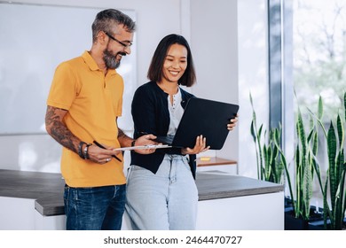 Portrait of an asian chinese business woman and a caucasian tattooed business man working together in a modern office. Couple of diverse business people using laptop together in the co-working space. - Powered by Shutterstock