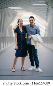 Portrait Of An Asian Chinese Couple On A Date Over The Weekend. The Man Is Young, Handsome And Well-dressed And The Woman Is Wearing An Elegant Summer Dress. They Are Smiling On A Bridge.