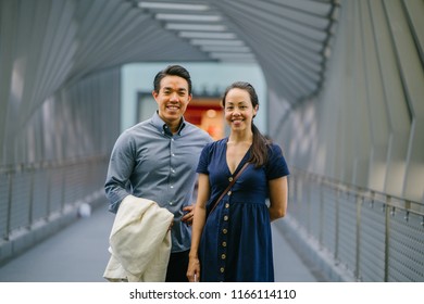 Portrait of an Asian Chinese couple on a date over the weekend. The man is young, handsome and well-dressed and the woman is wearing an elegant summer dress. They are smiling on a bridge.