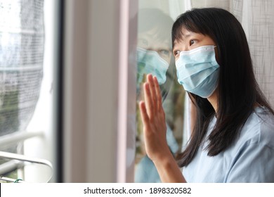 Portrait of an Asian Chinese female looking thru her balcony window with her face mask during the restricted movement order in Malaysia