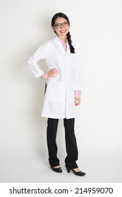 Portrait Of Asian Chinese Female Student In White Lab Uniform Smiling, Full Body Standing On Plain Background.