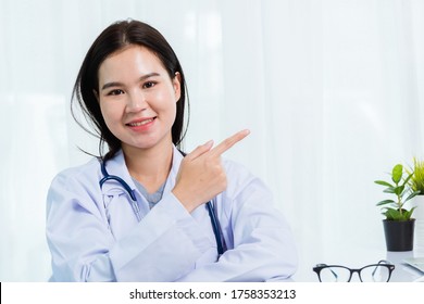 Portrait Asian Confident Female Doctor Working Personal Laptop Computer At Hospital Office. Thai Woman Medical Expertise Staff Smiling Her Point Finger To Side Away Space On Desk Space Front Computer