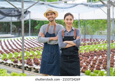 Portrait Of Asian Couple Farmers Work In Vegetables Hydroponic Farm. Attractive Agriculturist Young Man And Women Standing And Looking At Camera With Smiling And Confident At Green House Farm Together