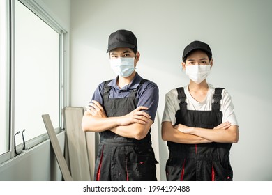 Portrait Of Asian Craftsman Or Carpenter Worker Man And Woman Wear Safety Helmet And Protective Mask, Crossed Arm And Look At Camera After Installs Laminate Board On Floor To Renovate House Apartment.