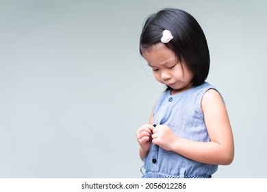 Portrait of Asian cute child girl is buttoning her shirt. Concept of doing daily activities, self-help. Copy space.