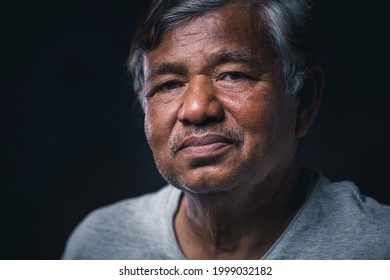 Portrait Of Asian Elderly Man Sitting Alone Looking At Camera On Dark Background, Wrinkled Skin, Gray Hair, 60+ Years Old.