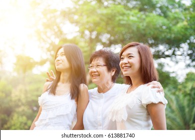 Portrait Of Asian Elderly Mother And Daughters Looking Away, Senior Adult Woman And Grown Child. Outdoors Family At Nature Park With Beautiful Sun Flare.