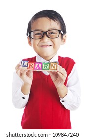 Portrait Of Asian Elementary School Student Showing Letter Blocks Spelling Out LEARN. Shot In Studio Isolated On White