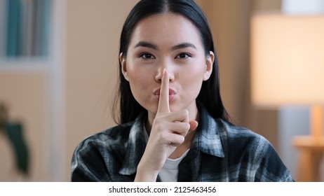 Portrait asian ethnic korean woman point with finger near mouth Chinese Japanese girl makes hush quiet gesture showing secret sign asks silent confidential secrecy information looking at camera indoor