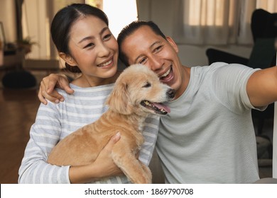 Portrait Of An Asian And European Couple Hugging A Dog For A Selfie With Their Mobile Phone. A Young Video Conference Call To Father And Mother. Face Time Concept