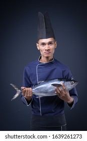 A Portrait Of An Asian Executive Chef In His Blue Uniform, Black Apron And Black Hat On Grey Background With A Skipjack Tuna