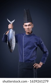 A Portrait Of An Asian Executive Chef In His Blue Uniform, Black Apron And Black Hat On Grey Background With A Skipjack Tuna